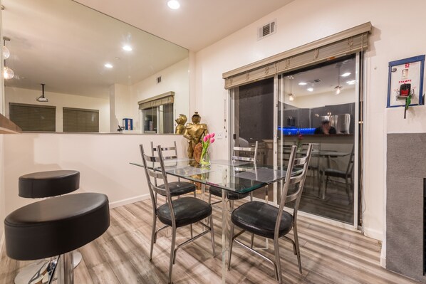 A modern dining area with a glass table and chairs, a decorative golden statue, and a view of the kitchen through a glass door.