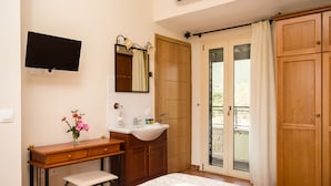 Un dormitorio con cama, un escritorio de madera con silla, tocador con espejo y televisor montado en la pared.