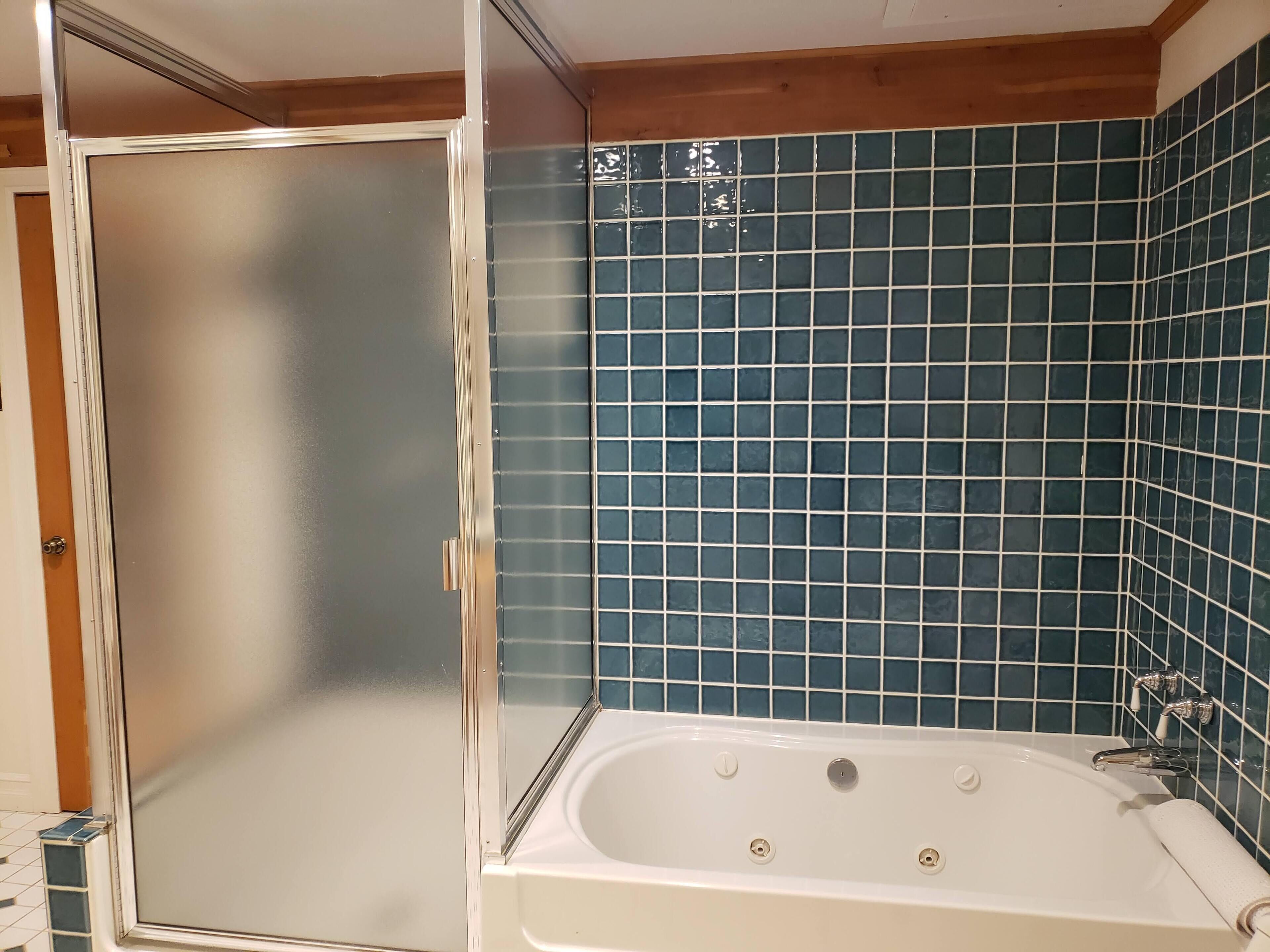 Un baño con cabina de ducha de vidrio, una bañera y paredes con azulejos azules.