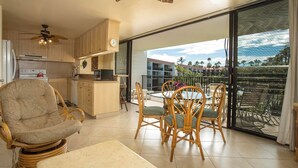 Amplia sala de estar con cocina, comedor y un balcón con vista a palmeras.