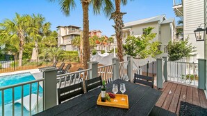A poolside table with a bottle of wine, glasses, and grapes, overlooking a pool and palm trees. - Forever Summer: Discover Your Happy Place! (Rosemary Beach)