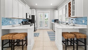 A modern kitchen with white cabinets, blue-tiled backsplash, and two bar stools. - Forever Summer: Discover Your Happy Place! (Rosemary Beach)