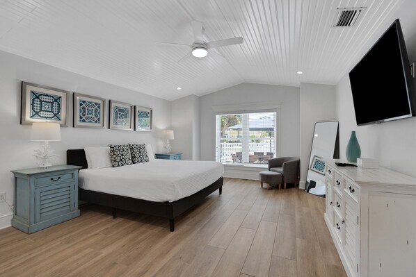 A bedroom with a bed, a ceiling fan, a TV, and a window with a view of the outside.