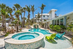 A swimming pool with a hot tub, surrounded by palm trees and lounge chairs.