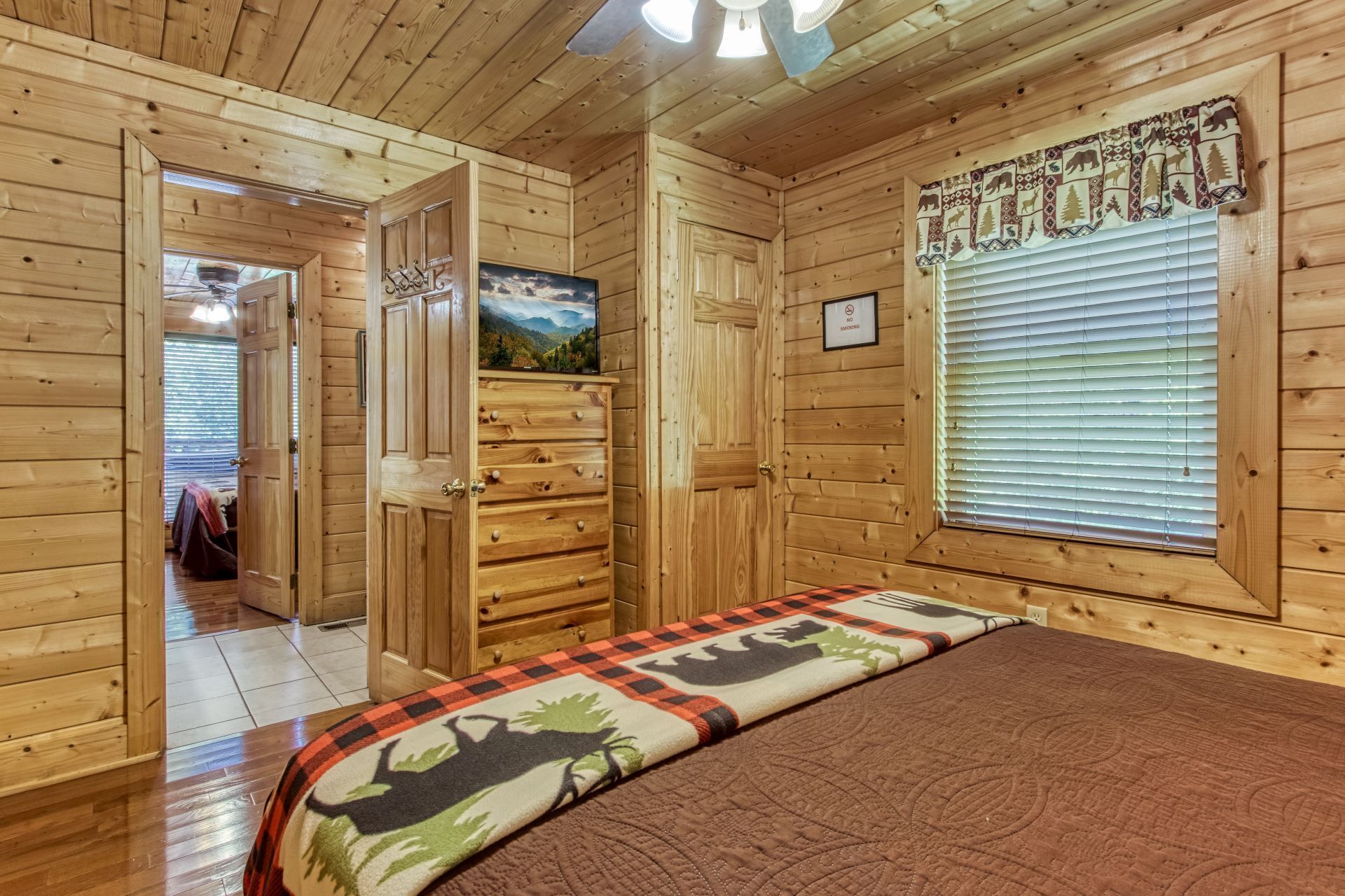 A wooden cabin room with a bed, a door leading to another room, and a window with blinds.