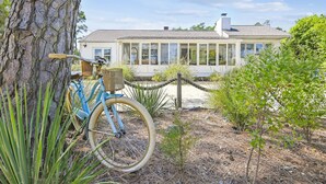 Una bicicleta estacionada cerca de un árbol, una casa con amplios ventanales y un jardín bien cuidado.