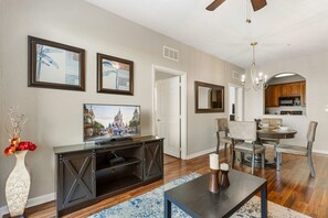 A living room with a television, a dining area with chairs, and a kitchen in the background.
