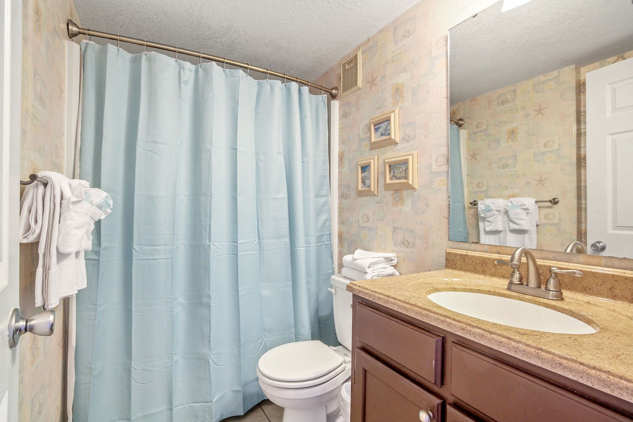 A bathroom with a shower curtain, toilet, sink, and mirror.