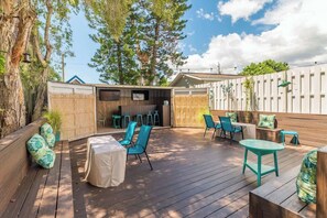 An outdoor patio with wooden flooring, blue chairs, and a covered table.