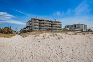 A beachfront hotel with multiple floors, balconies, and a sandy beach in the foreground.