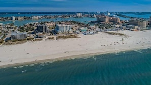An aerial view of a coastal city with a wide beach, buildings, and a marina.