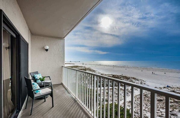 A balcony with a view of a beach, a chair, and a wall-mounted light fixture.