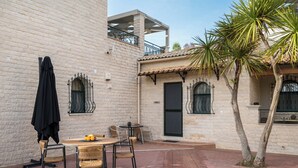 A courtyard with a brick wall, a table with chairs, a black umbrella, and a palm tree.