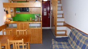 A compact room with a wooden dining table and chairs, a kitchenette with a green countertop, a red door, and a staircase. - Duplex 2-room, sleeps 6, ski-in/ski-out, Arc 1800, pets allowed (Les Arcs 1800)