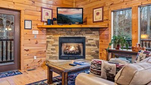 Ein gemütliches Blockhaus-Interieur mit Kamin aus Stein, Holzwänden, einem Fernseher und einer komfortablen Sitzecke.