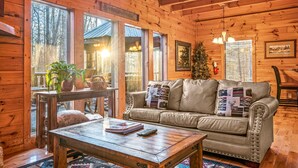 Ein gemütliches Blockhauss-Interieur mit Ledersofa, Holztisch und großem Fenster mit Blick auf einen Wald.