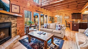 Ein gemütliches Blockhaus-Interieur mit Kamin aus Stein, Holzboden, einer Couch, einem Couchtisch und einer Küchenzeile.