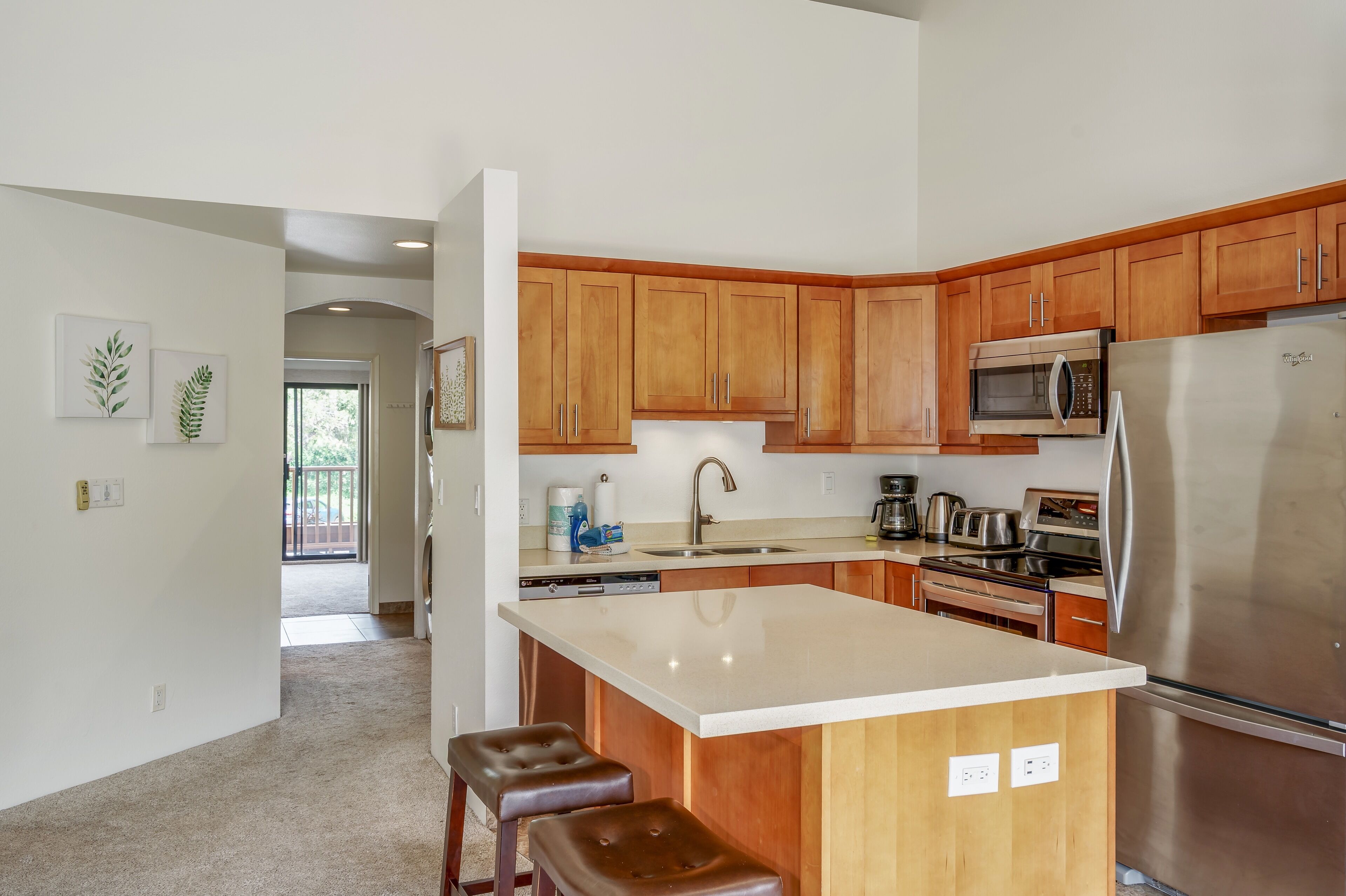 A modern kitchen with wooden cabinets, stainless steel appliances, and a central island with stools.