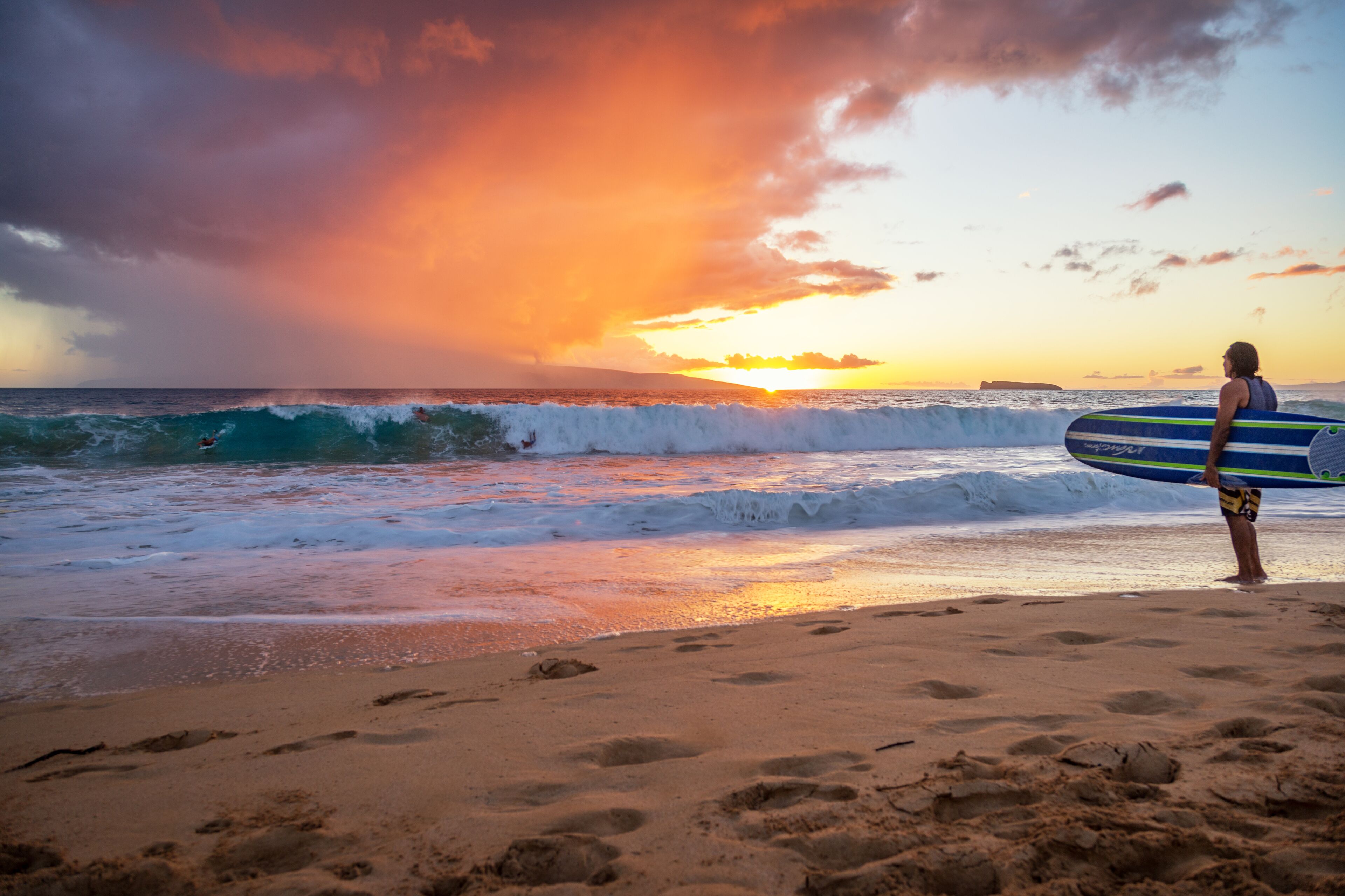 Escena de playa con olas y un atardecer.