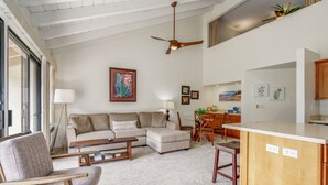Una sala de estar con sofá, sillón, mesa de centro, mesa de comedor con sillas y un área de cocina con mostrador y armarios.