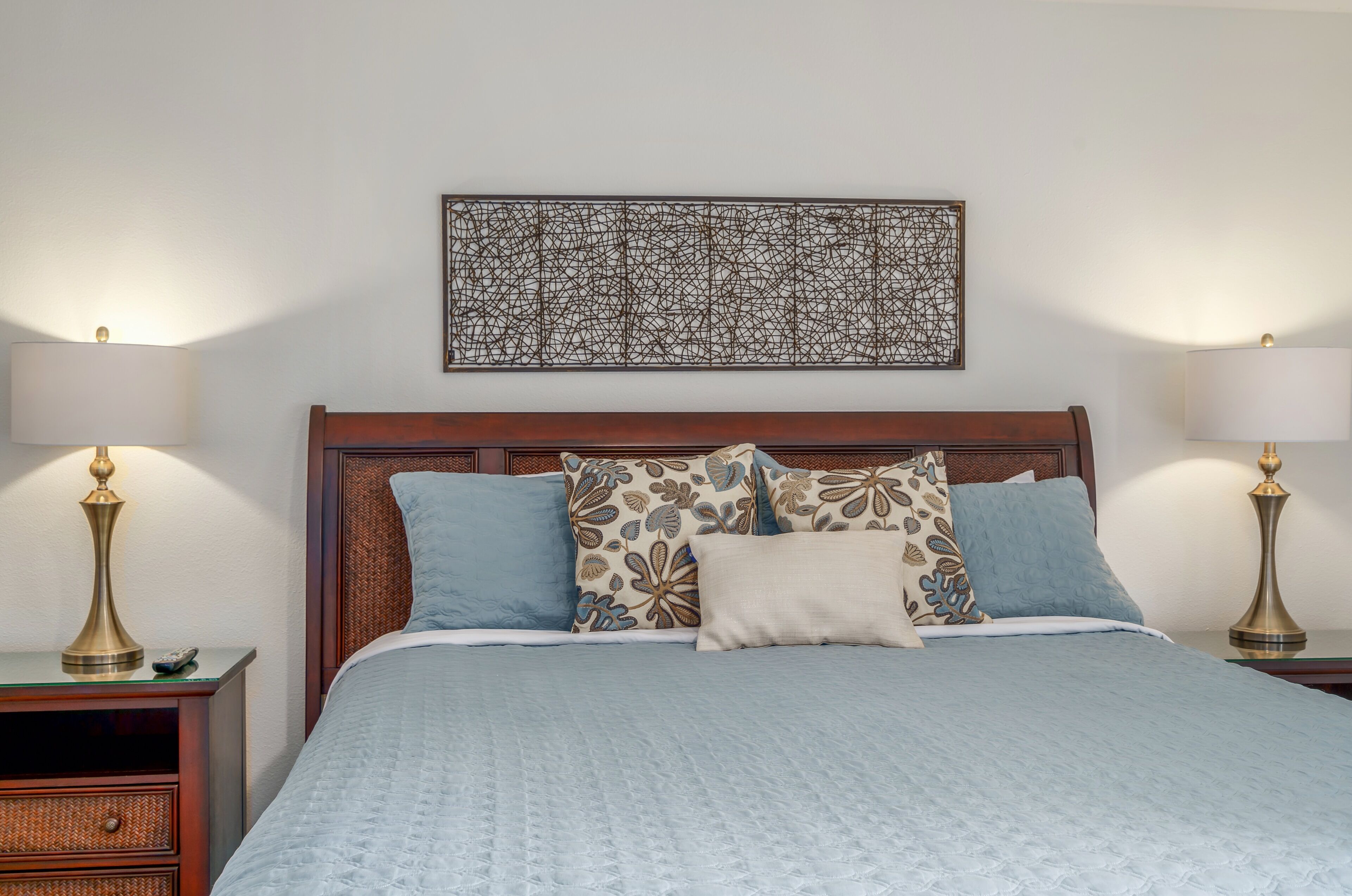 Una cama bien hecha con un cabecero estampado, dos lámparas de noche y una obra de arte colgada en la pared.