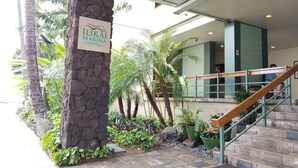 Un pilier en pierre surmonté d’une enseigne indiquant « ILIKAI MARINA », situé dans un hall d’entrée agrémenté d’un escalier, de palmiers et de plantes d’intérieur.
