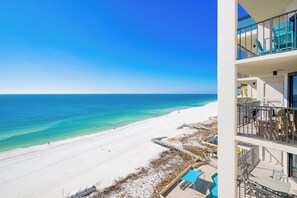 A beachfront hotel with a balcony overlooking the ocean, a pool area, and a beach access walkway.