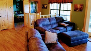 A cozy living room with a large sectional sofa, a wooden floor, and a view through a window.