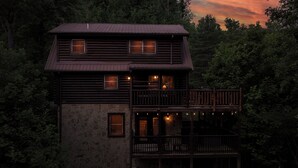 Eine zweistöckige Holzhütte mit Natursteinaußenwand, einem Balkon mit Geländern und zahlreichen Fenstern.