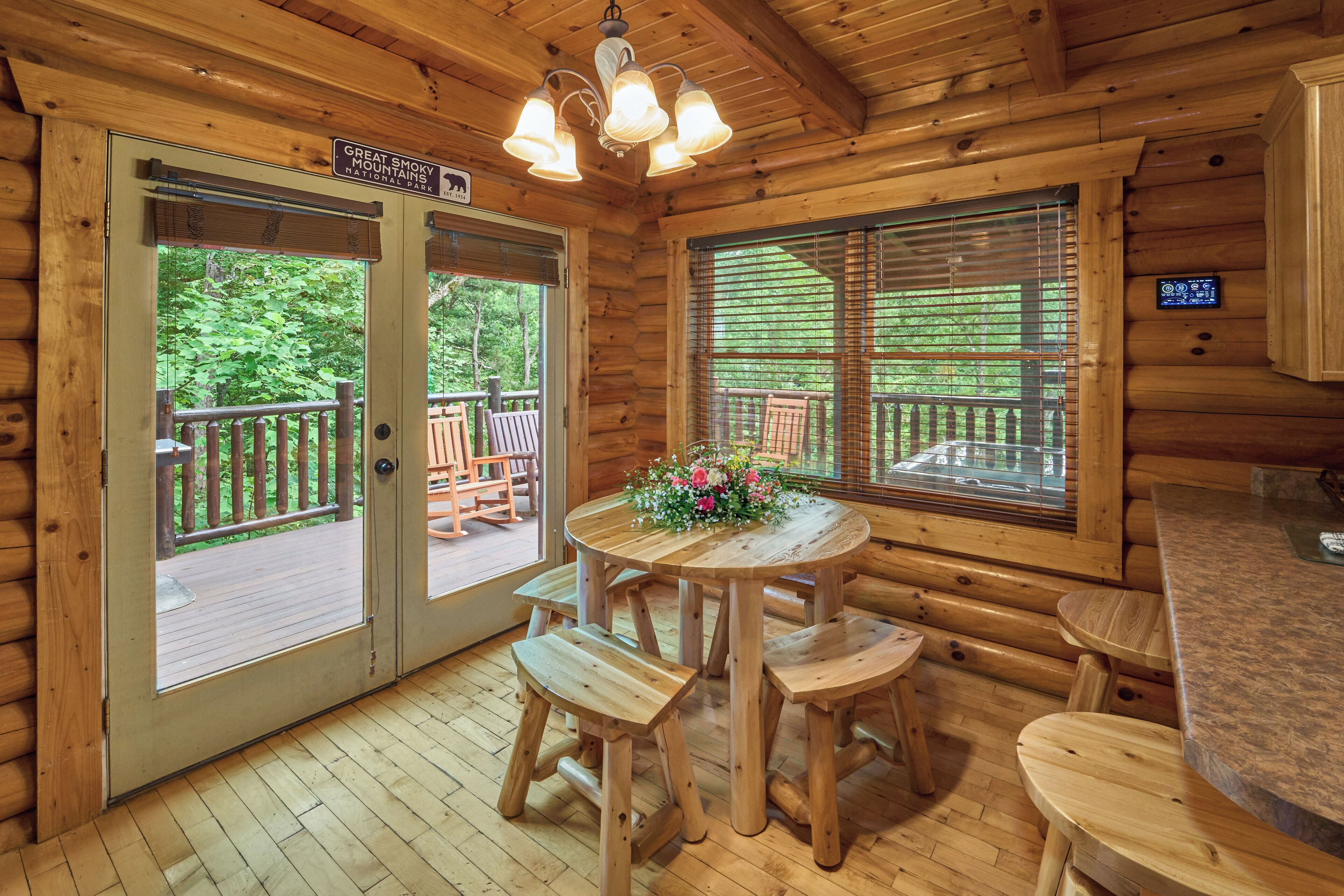 Een houten blokhut van binnen met een eettafel, vier houten stoelen, een klein rond tafeltje met een bloemenstuk en een bordje dat het Great Smoky Mountains National Park aangeeft.