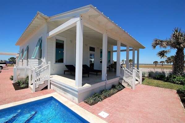A covered outdoor area with a pool, white columns, and a white fence.