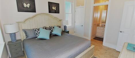 Un dormitorio con cama, mesitas de noche, ventilador de techo y baño visible a través de una puerta abierta.