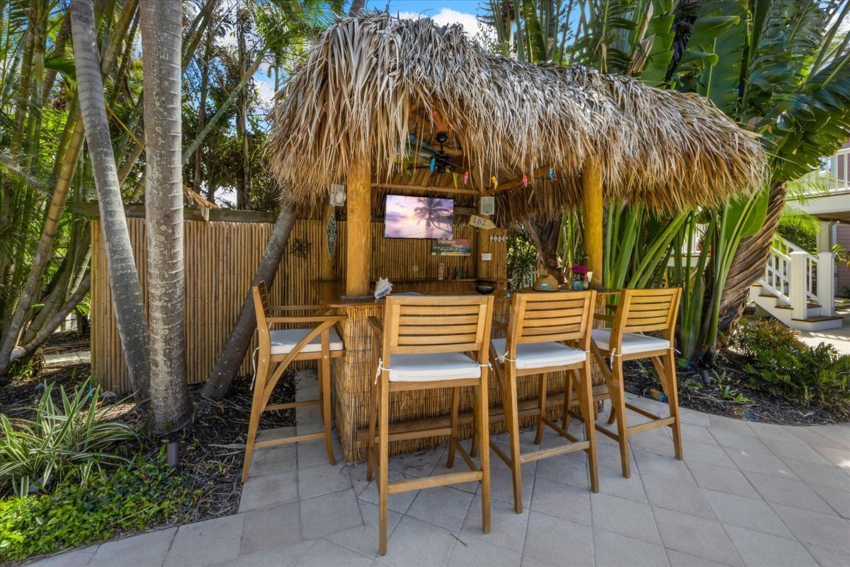 A thatched-roof outdoor bar area with wooden chairs and a television screen.