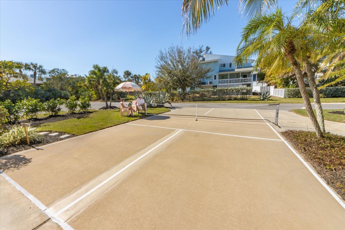 An outdoor tennis court with a net, surrounded by palm trees and greenery.