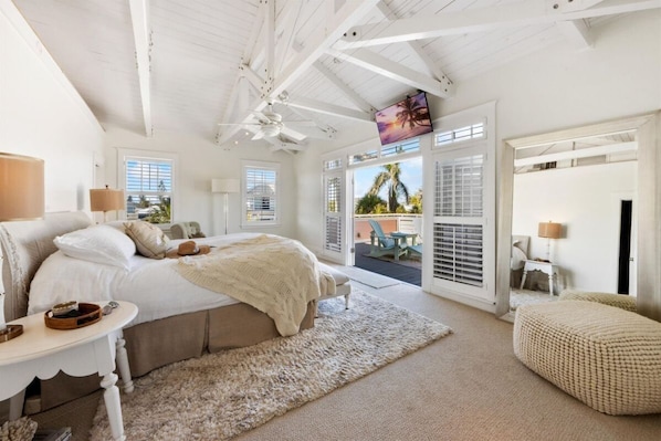 A bedroom with a large bed, a small table, a chair, and a view of the outdoors.