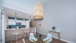 A modern kitchen with white cabinets, a dining area with a glass table and white chairs, and a hanging light fixture. - A17 Villas of Clearwater Beach Gulf-Front Condo (Clearwater Beach)