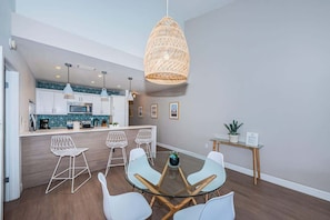 A modern kitchen with white cabinets, a dining area with a glass table and white chairs, and a hanging light fixture.