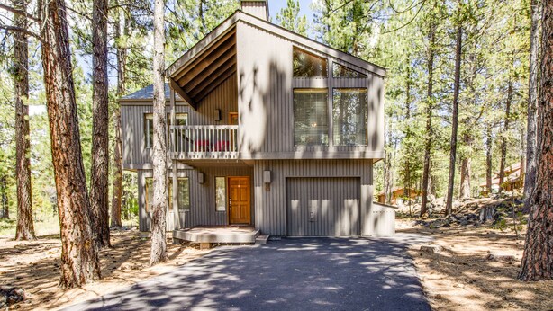 Een chalet met twee verdiepingen, een balkon, een garage en een oprit, omgeven door bomen.