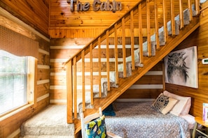 A cabin interior with a wooden staircase, a bed with patterned bedding, and a painting of an owl on the wall. - ER17 - The Perfect Getaway | Great location - Close to town! (Pigeon Forge)