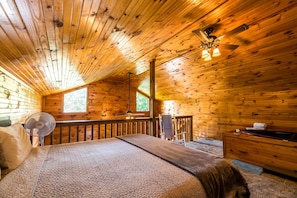 A cozy cabin with a wooden interior, a bed with a blanket, a fan, a desk, and a window. - ER17 - The Perfect Getaway | Great location - Close to town! (Pigeon Forge)