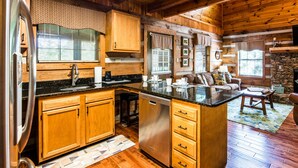 A kitchen with wooden cabinets, a stainless steel refrigerator, and a stone wall. - ER17 - The Perfect Getaway | Great location - Close to town! (Pigeon Forge)