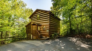 A wooden cabin with a porch and a small staircase, surrounded by dense green trees. - ER17 - The Perfect Getaway | Great location - Close to town! (Pigeon Forge)