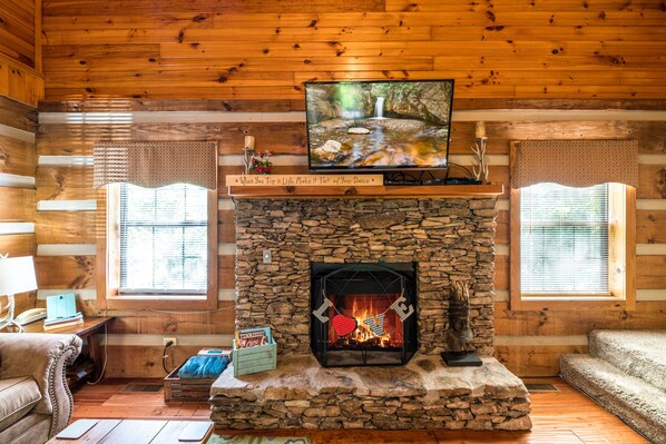 A log cabin interior with a stone fireplace, a television mounted above it, and a cozy seating area. - ER17 - The Perfect Getaway | Great location - Close to town! (Pigeon Forge)