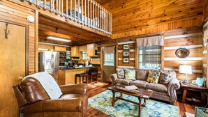 A cozy cabin interior with a wooden interior, a kitchen area, a living room with a sofa and coffee table, and a balcony with a railing. - ER17 - The Perfect Getaway | Great location - Close to town! (Pigeon Forge)