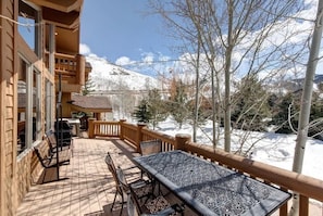 A wooden deck with a table and chairs, overlooking a snowy mountain. - Abode at Arrowood, 3 private master suites, hot tub, Deer Valley (Park City)