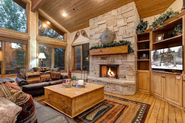 Una sala de estar acogedora con chimenea de piedra, mobiliario de cuero y ventanas amplias.