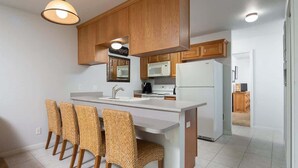 A kitchen with wooden cabinets, a white island with bar stools, a microwave, and a refrigerator. - WW C301 Urban Bungalow (New Braunfels)