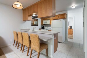 A kitchen with wooden cabinets, a white island with bar stools, a microwave, and a refrigerator.