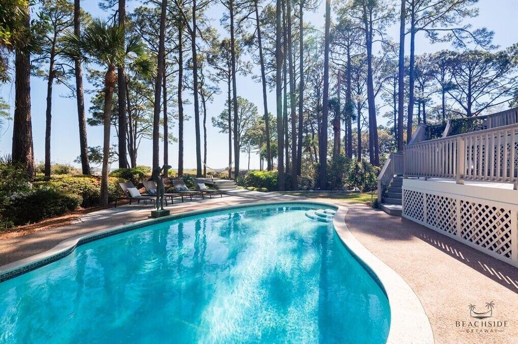 Una piscina rodeada de altos árboles y una cerca blanca.