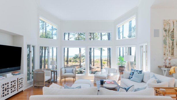 A spacious living room with a large TV, comfortable seating, and large windows offering a view of the outdoors.